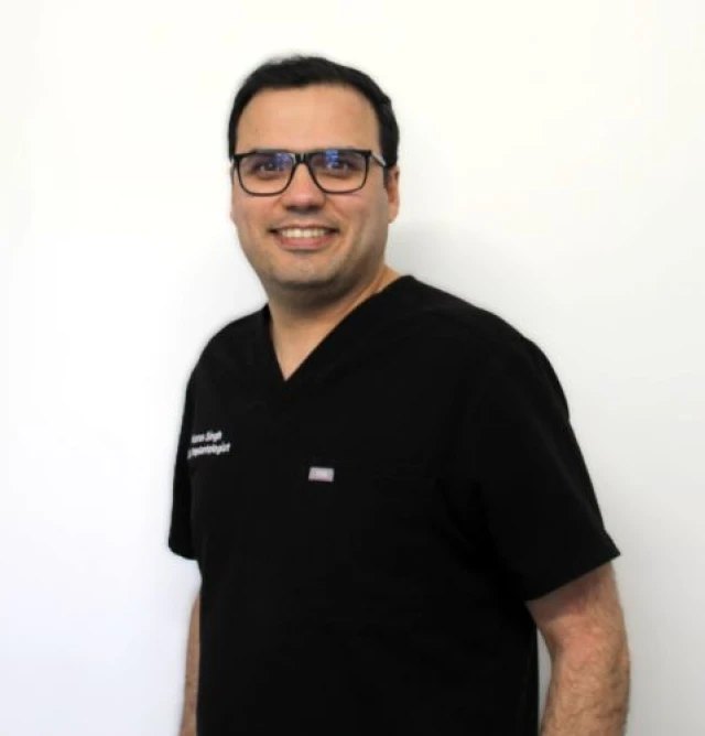 Dr Karan Singh standing in clinic, wearing black scrubs and glasses